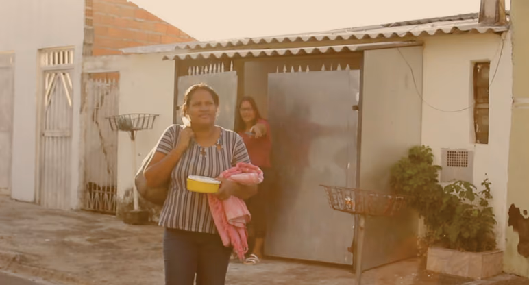 Cena do filme, mostra duas mulheres uma esta a frente carregando algumas coisas e a outra aparece no portão apontando