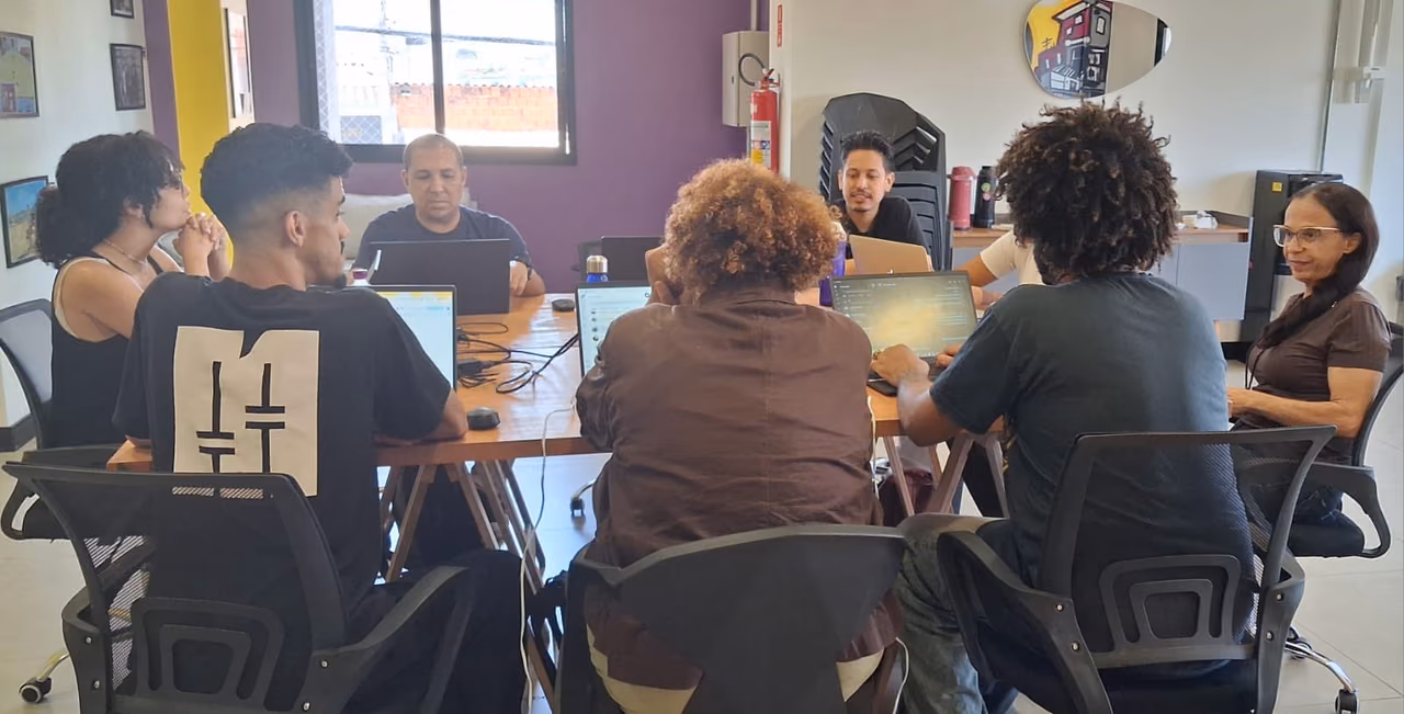 Participantes de um encontro de trabalho utilizando computadores e compartilhando informações para alinhar atividades e encaminhamentos.