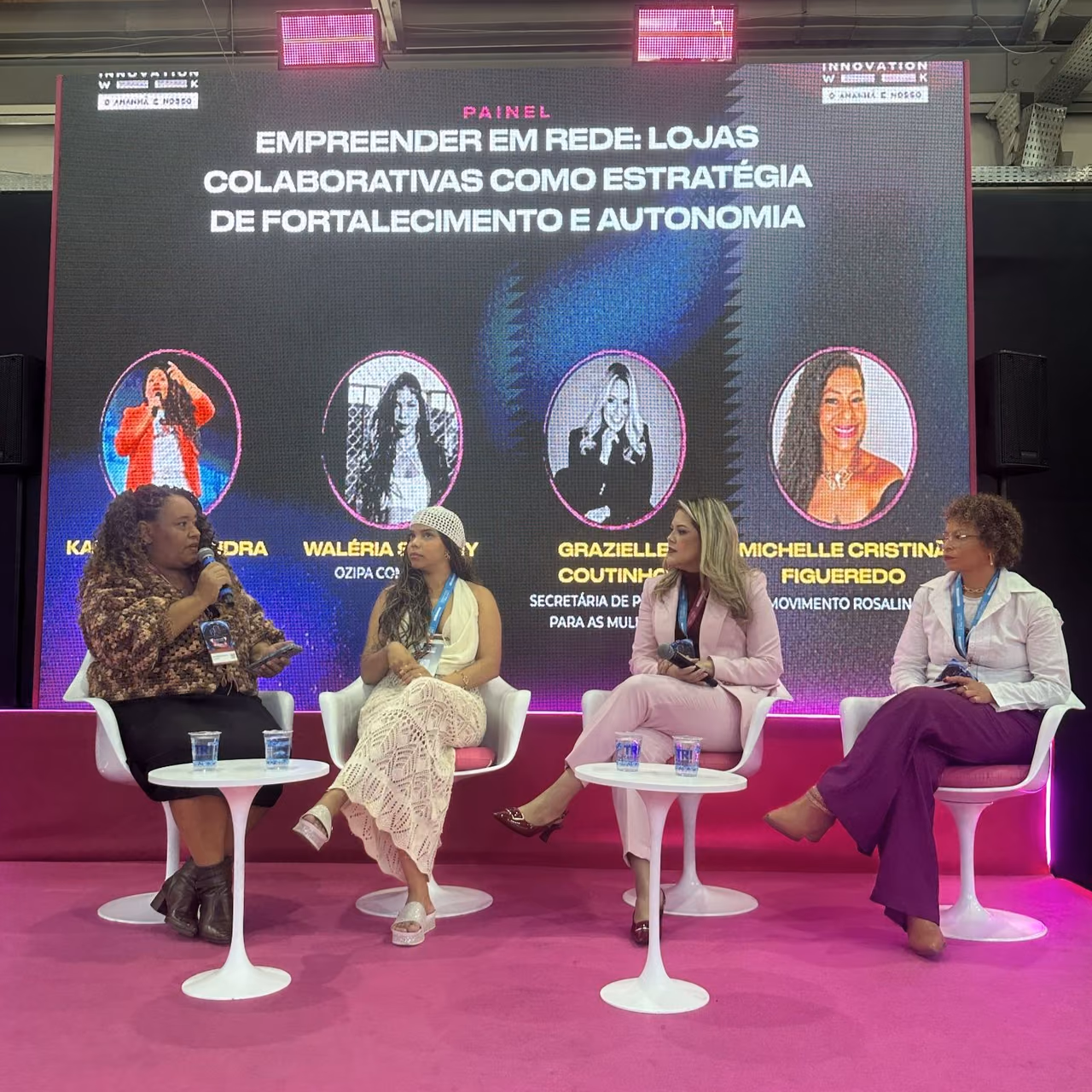 Four women participate in a conversation circle on the stage at Campinas Innovation Week 2026. Karla Marques is on the left, holding a microphone, alongside three participants. In the background, a panel features the theme “Networking entrepreneurship: collaborative stores as a strategy for strengthening and autonomy”.