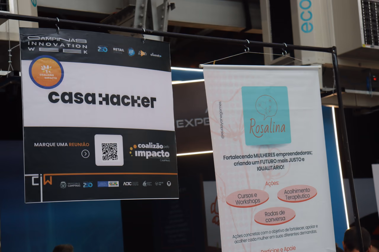 Two hanging banners in a space at Campinas Innovation Week 2024. On the left, a Casa Hacker banner identifying the Coalizão pelo Impacto Campinas. On the right, a Movimento Rosalina banner presents actions aimed at strengthening women entrepreneurs, such as courses, workshops, therapeutic support, and conversation circles.
