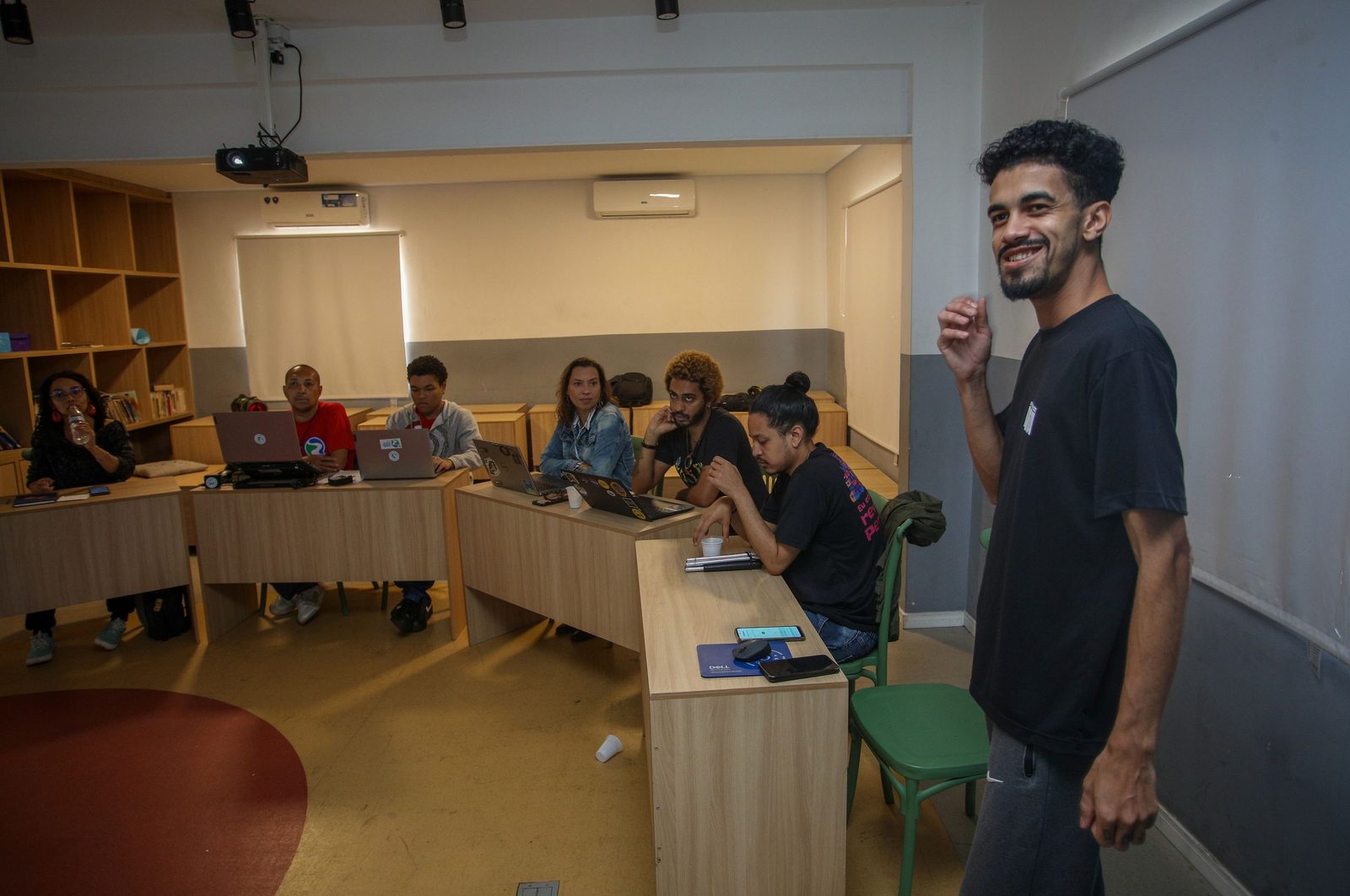 Facilitador conduz atividade formativa em sala de aula enquanto participantes acompanham a apresentação com notebooks e materiais de apoio.