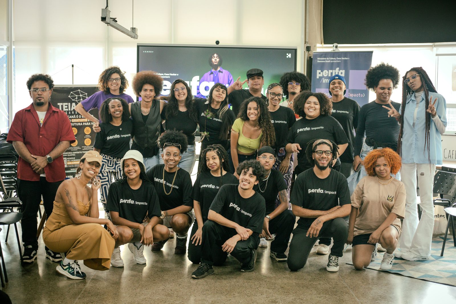 Turma do PerifaImpacto em São Paulo posa para foto vestindo camisetas pretas do programa, entre banners do projeto.