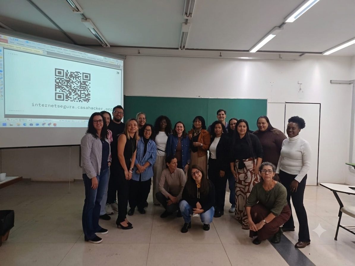 Turma de conselheiras e conselheiros tutelares posa em sala de aula diante do telão com o QR code do site Internet Segura da Casa Hacker.