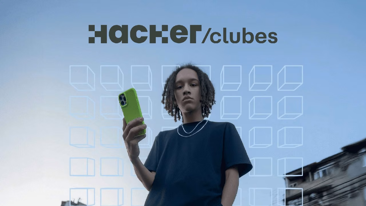 Jovem segura o celular sob o céu aberto, com a marca Hackerclubes no alto da peça.